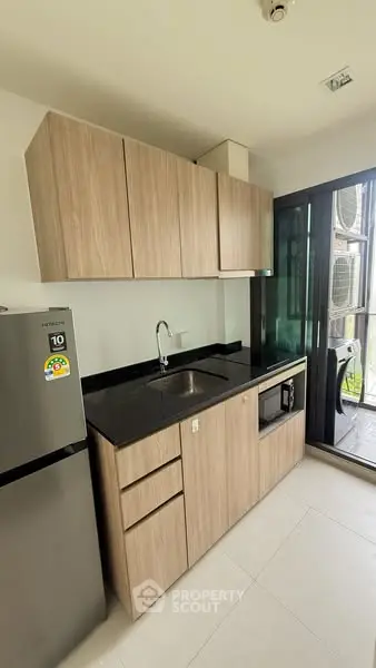 Modern compact kitchen with sleek wooden cabinets and black countertop in a bright apartment.