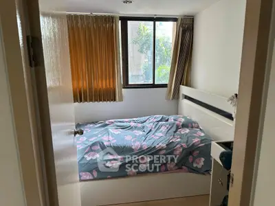 Cozy bedroom with floral bedding and large window offering natural light.