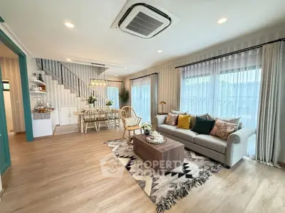 Spacious living room with modern decor and open dining area, featuring large windows and stylish furnishings.