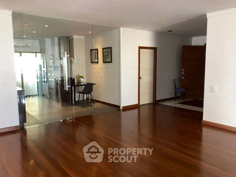 Spacious open-plan living area with wooden flooring and glass partition.