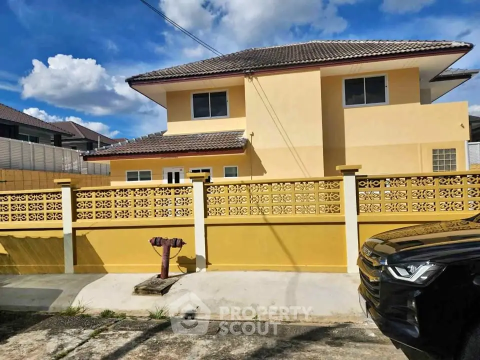 Charming two-story yellow house with decorative fence and driveway, perfect for family living.