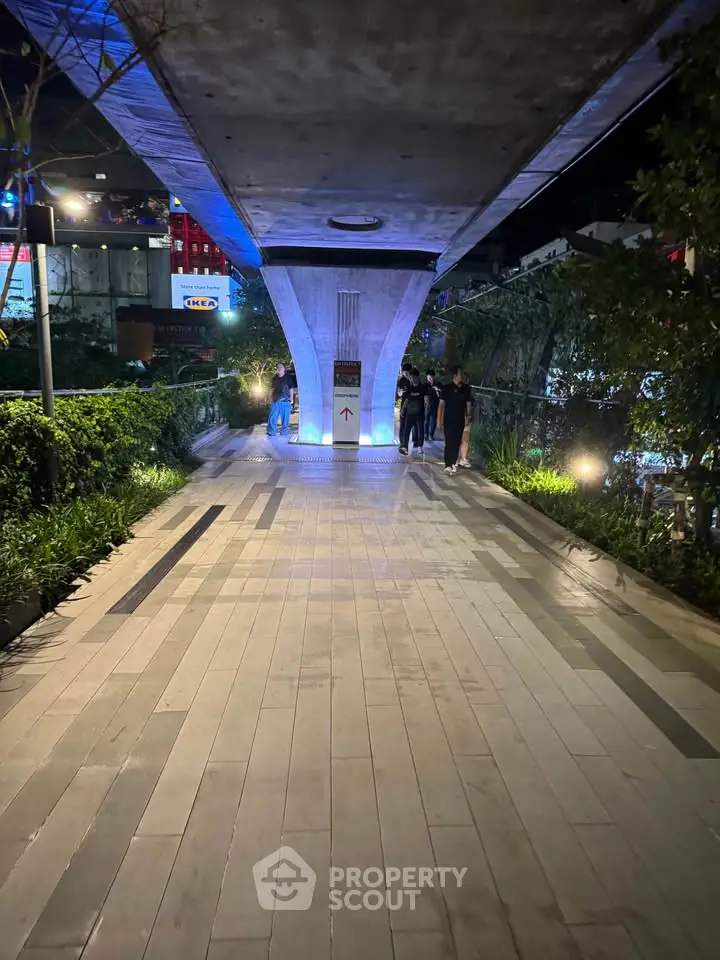 Modern urban walkway with ambient lighting and lush greenery at night.