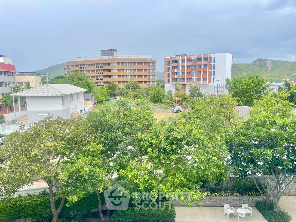 Scenic view of modern residential buildings surrounded by lush greenery and mountains.