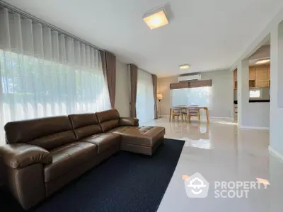 Spacious modern living room with leather sofa and dining area, featuring large windows and elegant decor.