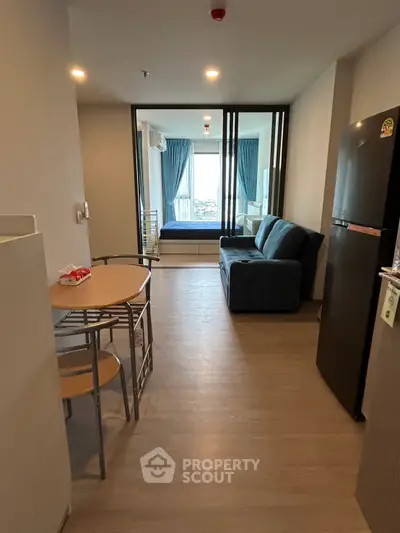 Modern open-plan living room with dining area and view into bedroom, featuring sleek furniture and natural light.