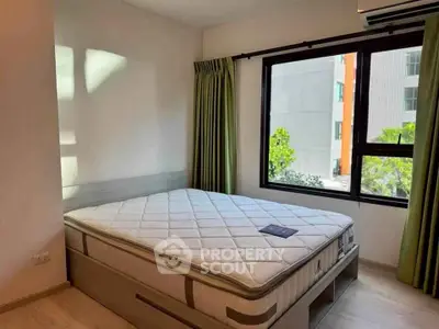 Bright bedroom with large window and green curtains, featuring a comfortable mattress on a wooden bed frame.