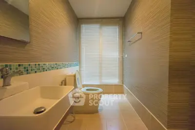 Modern bathroom with stylish sink and toilet, featuring elegant wall tiles and natural light.
