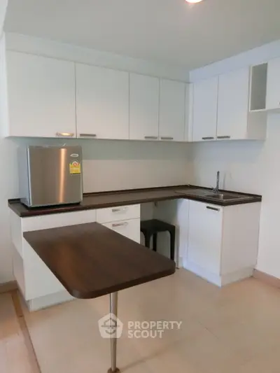 Modern kitchen with sleek white cabinets and compact fridge in open layout design.