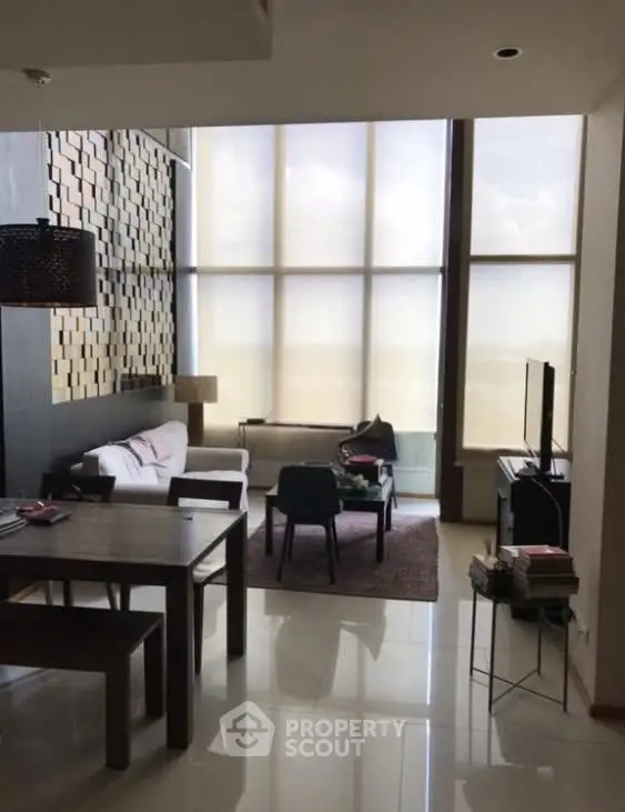 Modern living room with high ceilings and large windows, featuring stylish furniture and decor.
