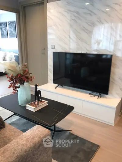 Modern living room with stylish decor and flat-screen TV, featuring elegant marble wall design.