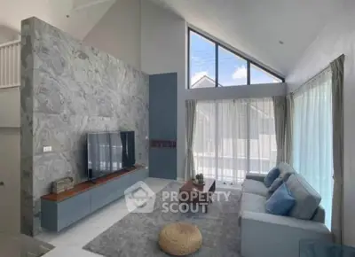 Modern living room with high ceiling and large windows, featuring stylish decor and natural light.