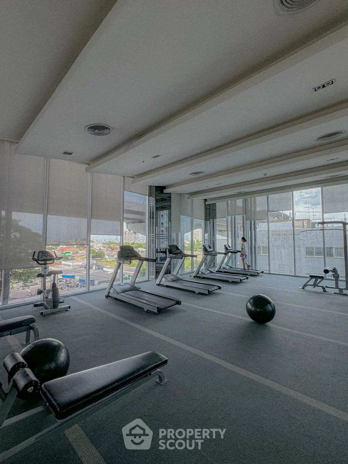 Spacious gym with modern equipment and city view, perfect for fitness enthusiasts.