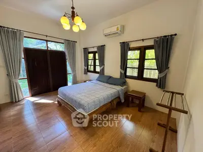 Spacious bedroom with wooden flooring and large windows offering natural light.