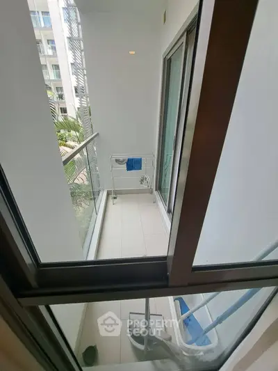 Modern apartment balcony with glass railing and laundry rack, offering a compact outdoor space.