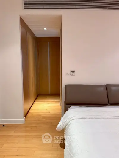 Modern bedroom with wooden flooring and sleek design, featuring a cozy bed and built-in wardrobe.