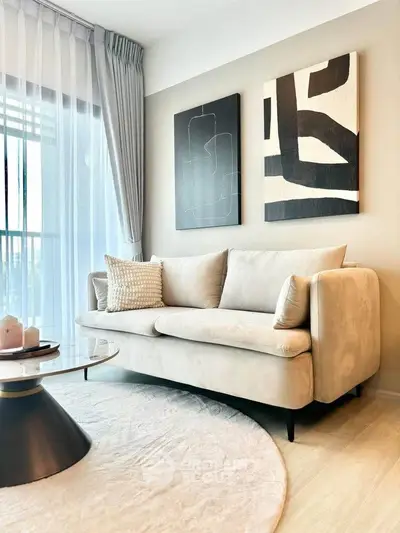 Modern living room with elegant beige sofa and abstract art, featuring floor-to-ceiling windows and chic decor.