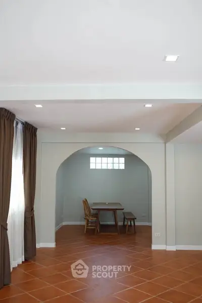 Spacious living area with terracotta tiles and archway leading to dining space, perfect for family gatherings.