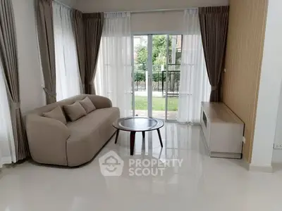 Elegant living room with modern sofa and coffee table, featuring large windows and garden view.