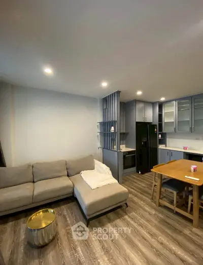 Modern living room with open kitchen, featuring sleek cabinetry and cozy seating area.
