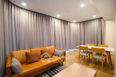 Modern living room with stylish leather sofa and dining area, featuring elegant lighting and floor-to-ceiling curtains.
