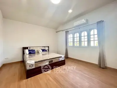 Spacious bedroom with wooden flooring and large windows in a modern home.
