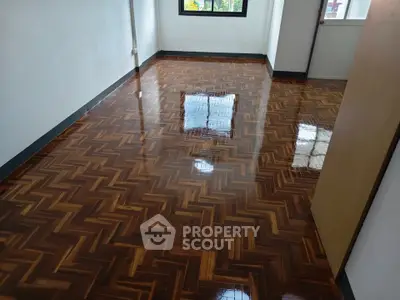 Spacious room with polished wooden flooring and natural light from large window.