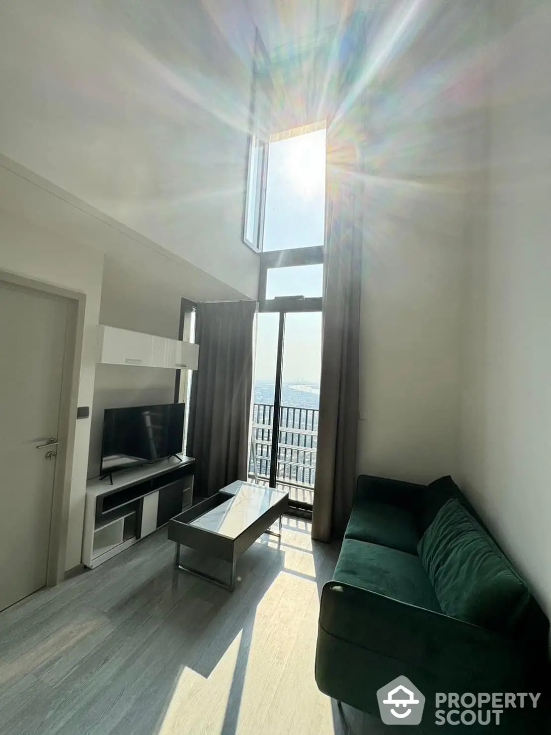 Sun-drenched modern living room with floor-to-ceiling windows offering a panoramic city view, complemented by sleek furnishings and a cozy layout.