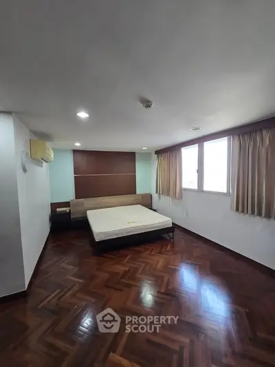Spacious bedroom with wooden flooring and large windows for natural light.