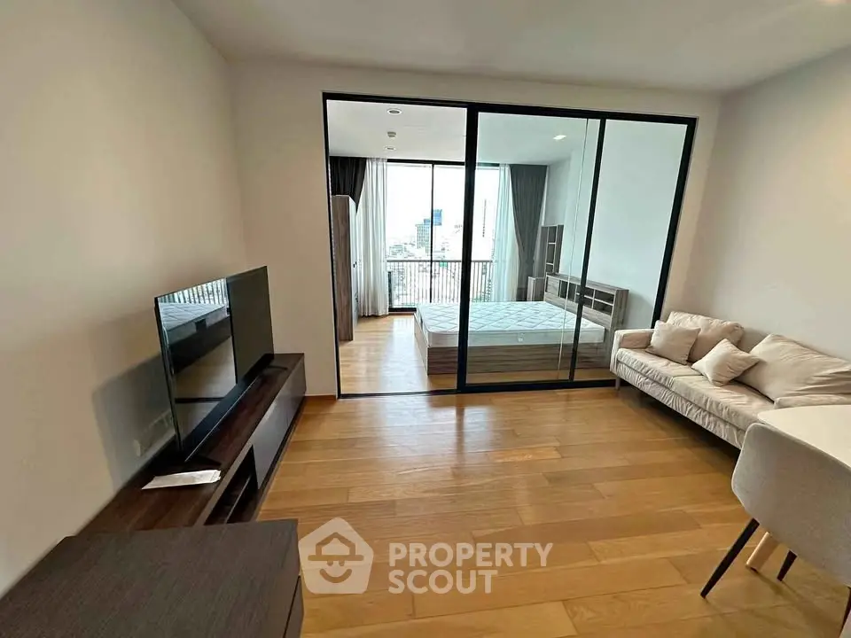 Modern apartment with open living room and bedroom, featuring sleek furniture and city view.