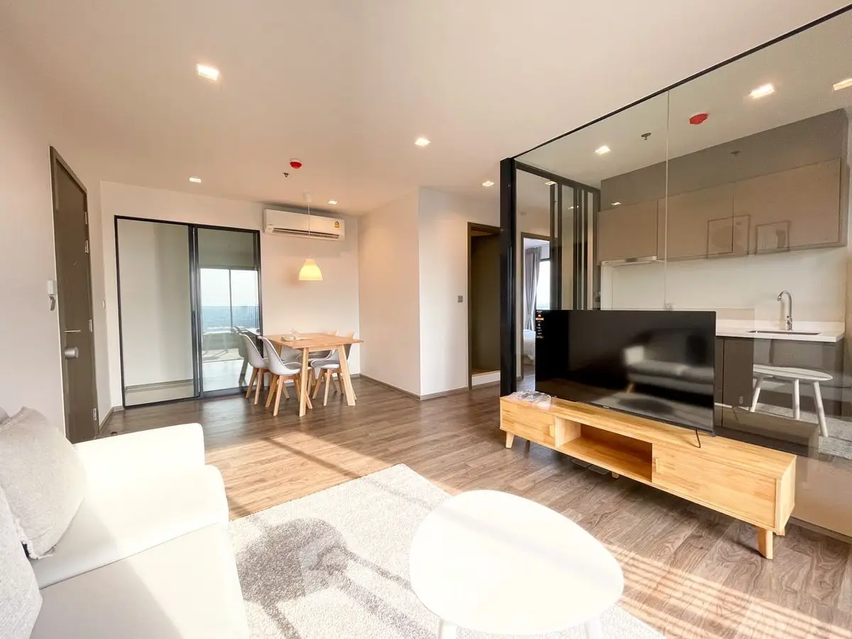 Modern living room with open kitchen and dining area, featuring sleek furniture and natural light.
