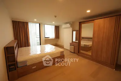 Spacious bedroom with wooden furniture and large window offering natural light.