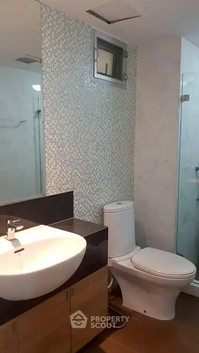 Modern bathroom with stylish sink and toilet, featuring elegant tile design and glass shower enclosure.