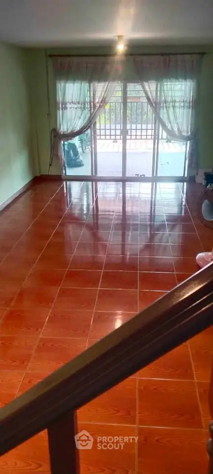 Spacious living room with polished wooden floors and large windows leading to a balcony.
