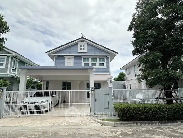 Charming two-story blue house with gated driveway and lush greenery in a serene neighborhood.