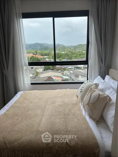Cozy bedroom with scenic window view of lush green hills and town.