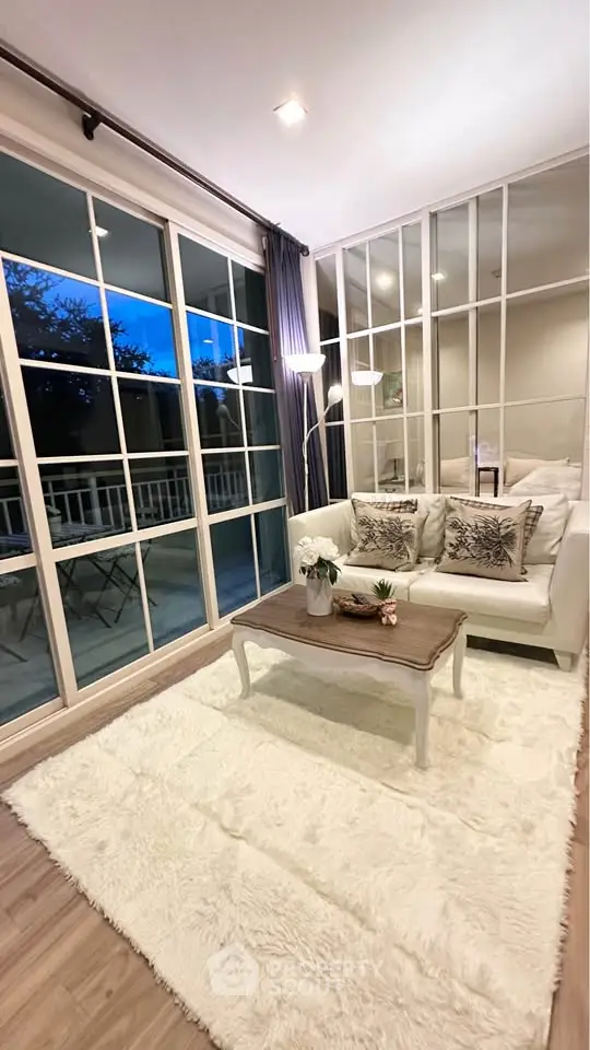 Elegant living room with large windows and cozy decor, featuring a plush rug and stylish furniture.