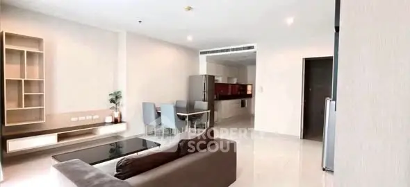 Spacious modern living room with open kitchen and dining area, featuring sleek furniture and bright lighting.