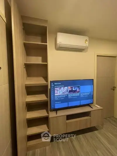 Modern living room with built-in wooden shelves and air conditioning unit, featuring a sleek TV setup.