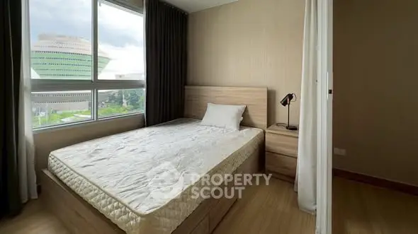 Cozy bedroom with large window and modern furnishings, offering a serene view.