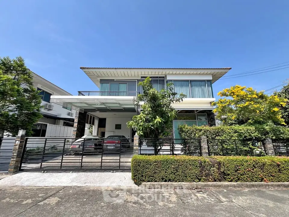 Modern two-story house with large windows and lush greenery in a suburban setting.