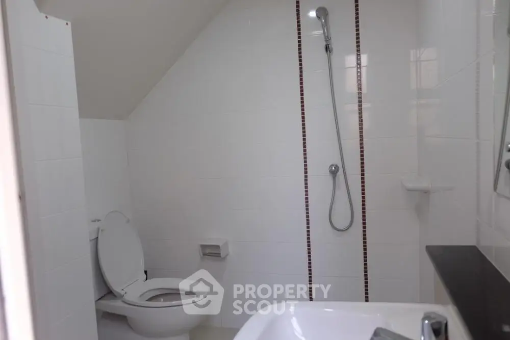 Sleek modern bathroom with wall-mounted toilet, spacious shower area, and elegant bathtub under a sloped ceiling, perfect for contemporary living.
