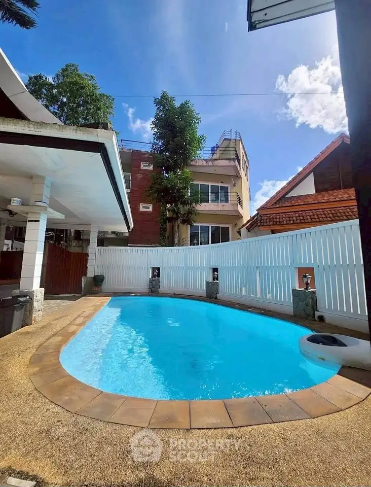 Charming outdoor pool area with clear blue water, surrounded by a white fence and lush greenery, perfect for relaxation.