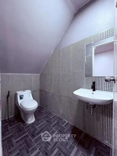Modern bathroom with sleek design and geometric tiles, featuring a wall-mounted sink and toilet.