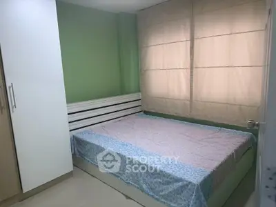 Cozy bedroom with green walls and large window, featuring a comfortable bed and ample storage space.