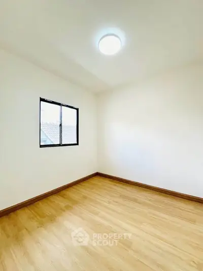 Bright empty room with wooden flooring and a window, perfect for customization.
