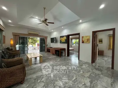 Spacious living room with marble flooring and ceiling fan, opening to a balcony with lush views.