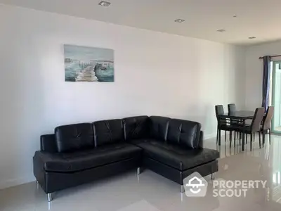 Modern living room with sleek black leather sectional and dining area, featuring glossy tile flooring and minimalist decor.