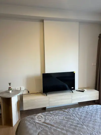 Modern bedroom with sleek TV stand and cozy bedding in a stylish apartment.