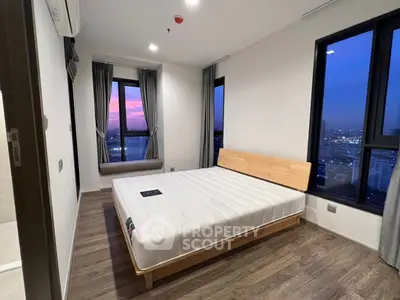 Modern bedroom with city view, featuring large windows and stylish wooden flooring.