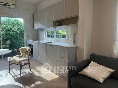 Modern kitchen with sleek cabinetry and natural light, featuring cozy seating and lush garden view.